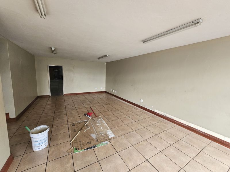 An empty industrial office or utility space featuring tiled flooring, fluorescent lighting, and neutral wall finishes.