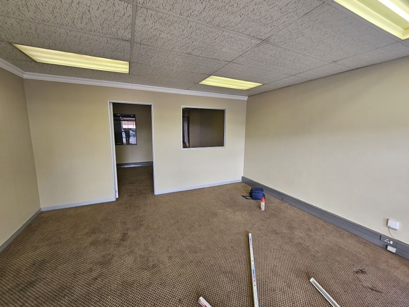 An empty office space featuring a suspended acoustic ceiling, recessed fluorescent lighting, and wall-to-wall carpeting with an internal window partition.