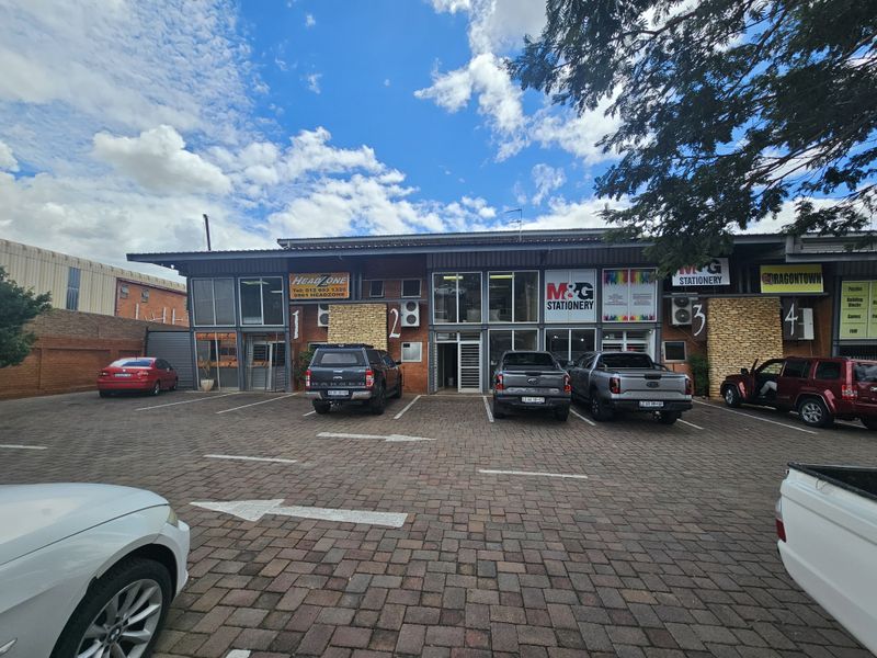 Front exterior view of a multi-unit industrial complex featuring paved parking, brick facade, and multiple commercial signage displays.