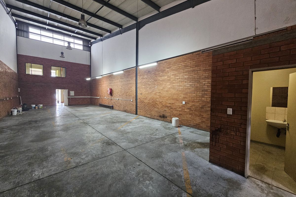 Spacious industrial warehouse unit featuring high ceilings, exposed brick walls, concrete flooring, and an integrated restroom facility.