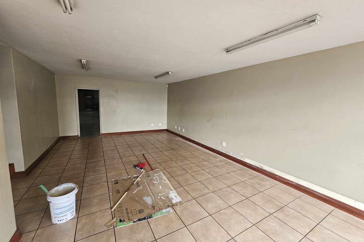 An empty industrial office or utility space featuring tiled flooring, fluorescent lighting, and neutral wall finishes.