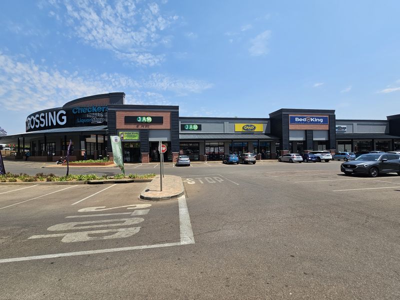 A wide-angle view of a modern retail shopping center exterior featuring multiple storefronts, paved parking area, and clear signage.
