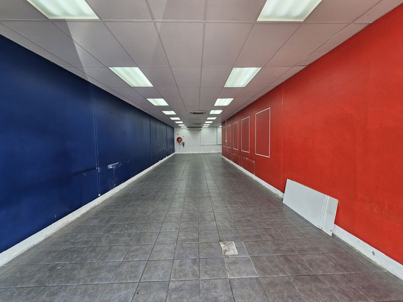 An empty retail space featuring tiled flooring, recessed ceiling lighting, and high-contrast red and blue painted walls, suitable for a variety of commercial uses.