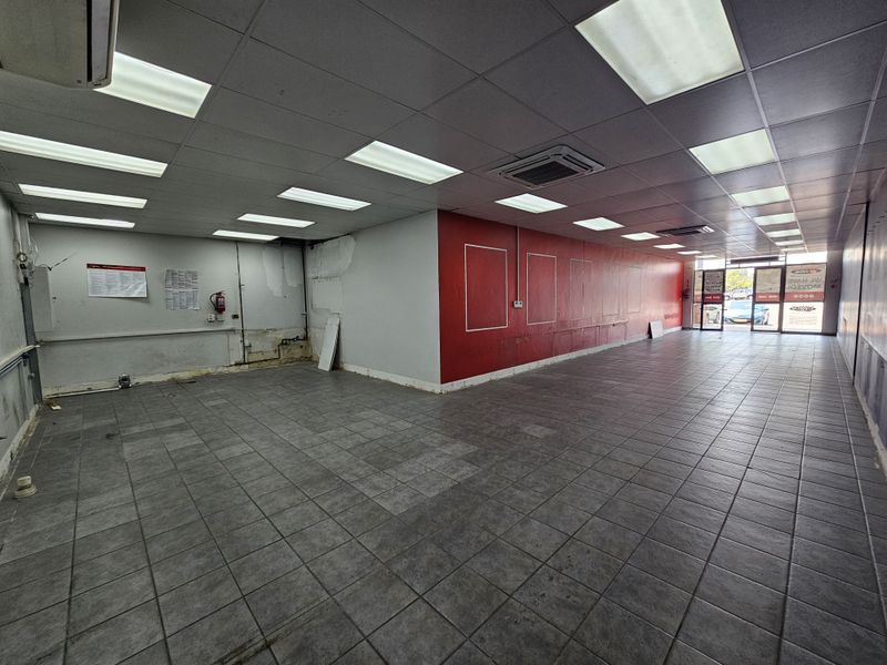 An empty retail space featuring tiled flooring, a suspended ceiling with recessed lighting, and a prominent red feature wall.