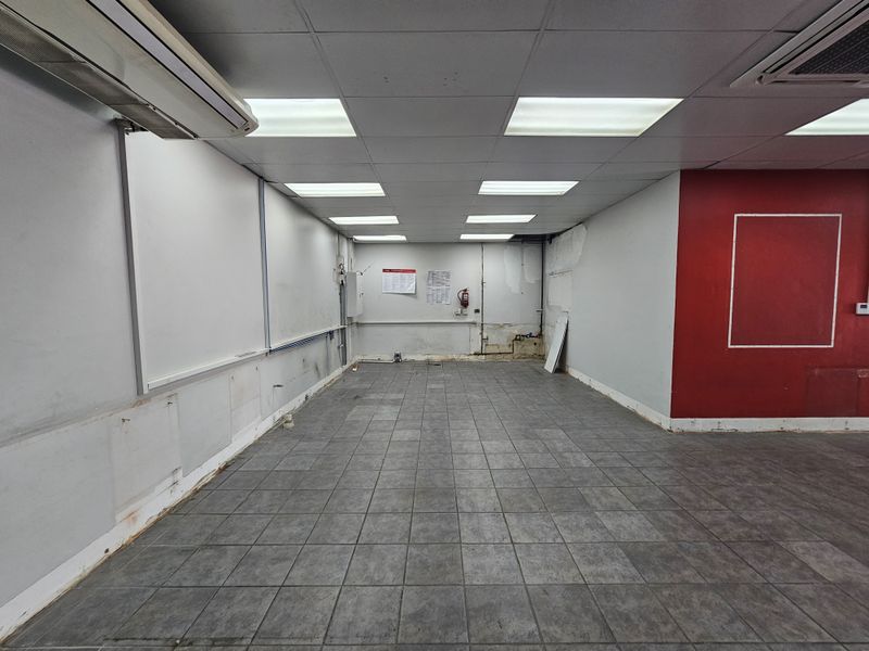 An empty retail space featuring tiled flooring, a suspended ceiling with recessed lighting, and an integrated air conditioning unit.