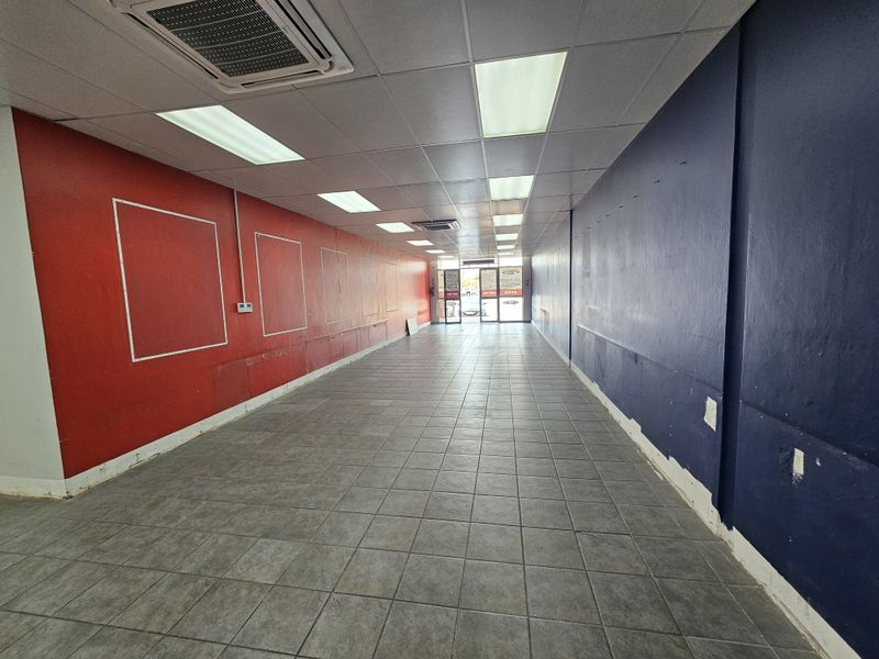 An empty retail space featuring tiled flooring, recessed ceiling lighting, and a central air conditioning unit, ready for custom fit-out.
