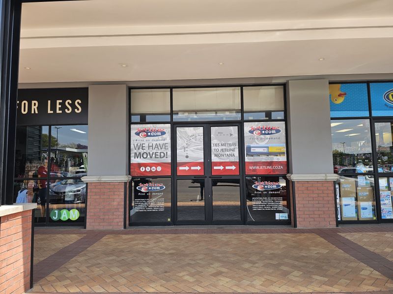 Retail storefront entrance featuring large glass display windows and double glass doors with brick facade detailing under a covered walkway.