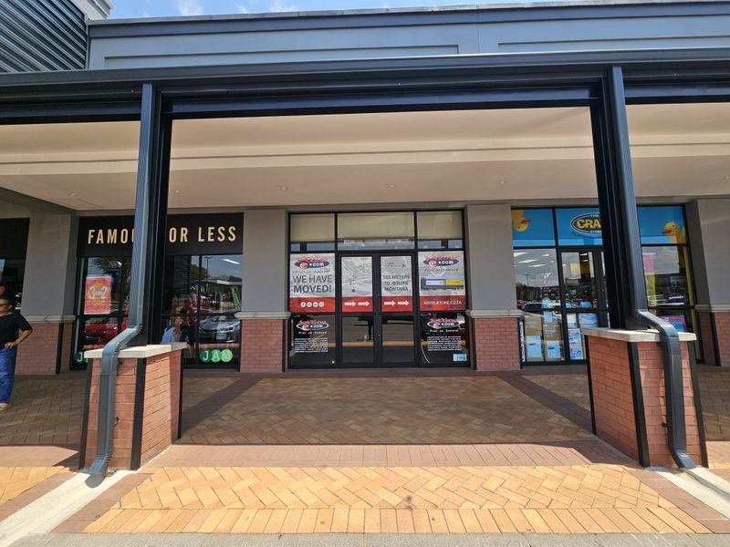 A retail storefront entrance featuring a covered walkway with brick paving, glass display windows, and modern architectural framing.
