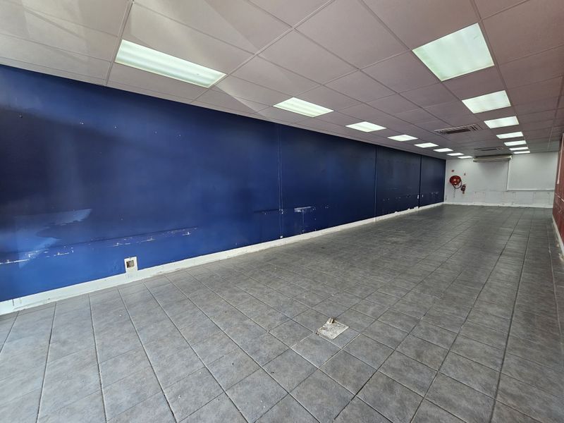 A spacious, empty retail unit featuring tiled flooring, recessed ceiling lighting, and a prominent blue feature wall, suitable for various commercial business applications.
