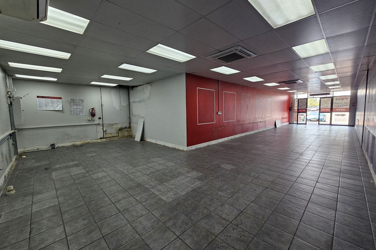 An empty retail space featuring tiled flooring, a suspended ceiling with recessed lighting, and a prominent red feature wall.
