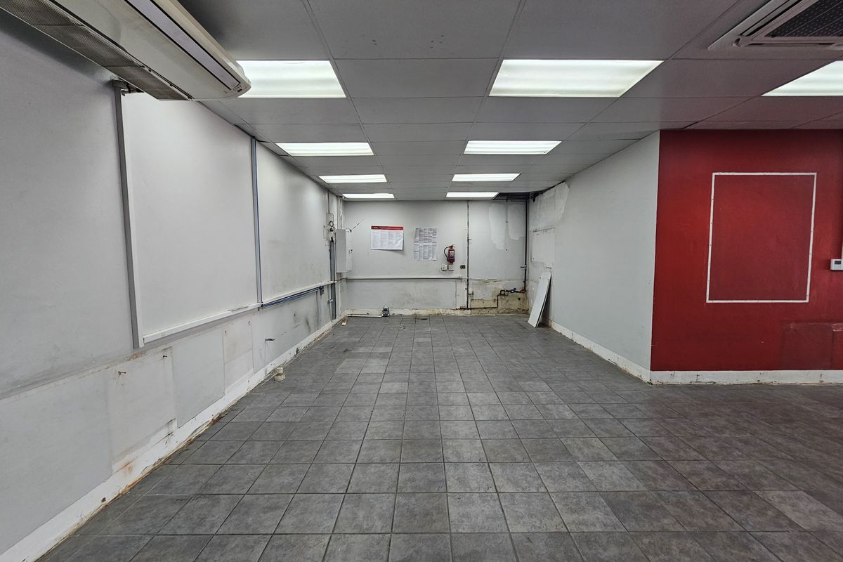 An empty retail space featuring tiled flooring, a suspended ceiling with recessed lighting, and an integrated air conditioning unit.