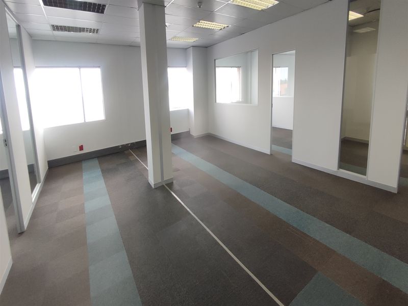 An empty, open-plan office space featuring carpet tiles, suspended ceilings with recessed lighting, and glass partition walls.