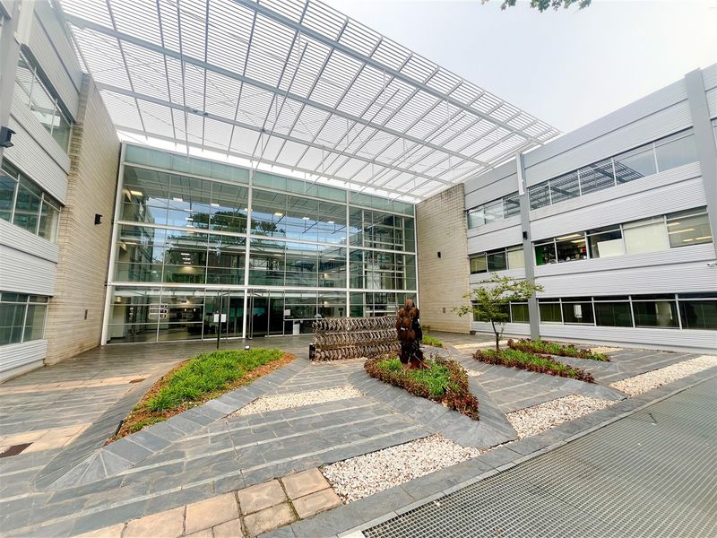 Modern office building courtyard featuring a large glass facade, metal louvered canopy, and professionally landscaped slate-paved outdoor area.