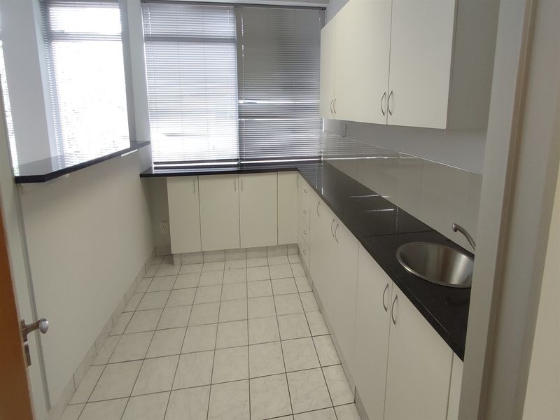 A clean, functional office kitchenette featuring white built-in cabinetry, dark granite countertops, a stainless steel sink, and tiled flooring.