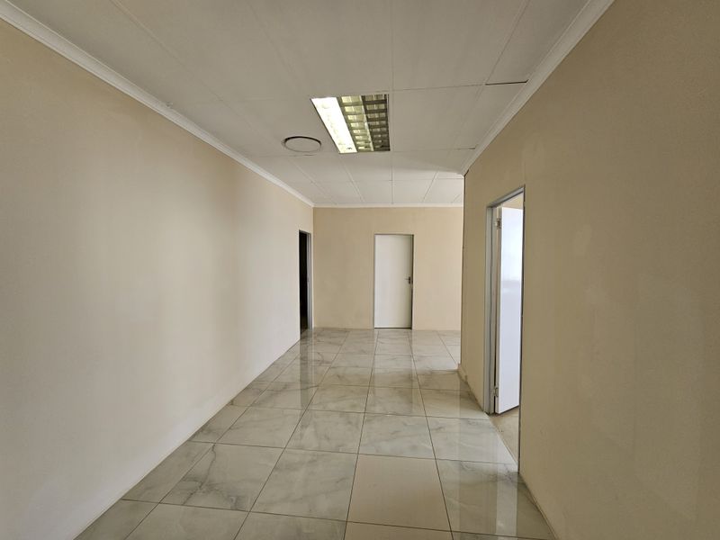 A bright, empty hallway featuring polished marble-look floor tiles, recessed ceiling lighting, and multiple doorways leading to adjacent rooms.