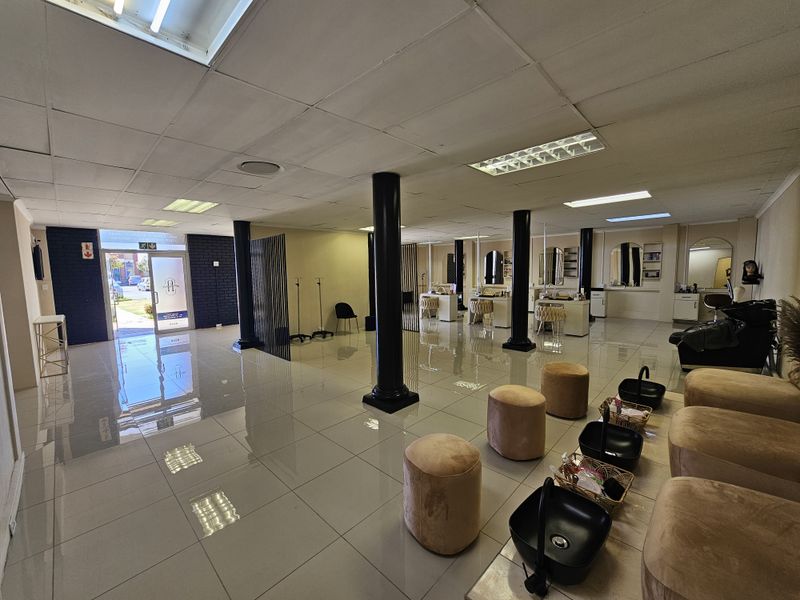 Spacious open-plan retail salon area featuring polished tile flooring, structural support columns, and recessed fluorescent lighting throughout the commercial space.