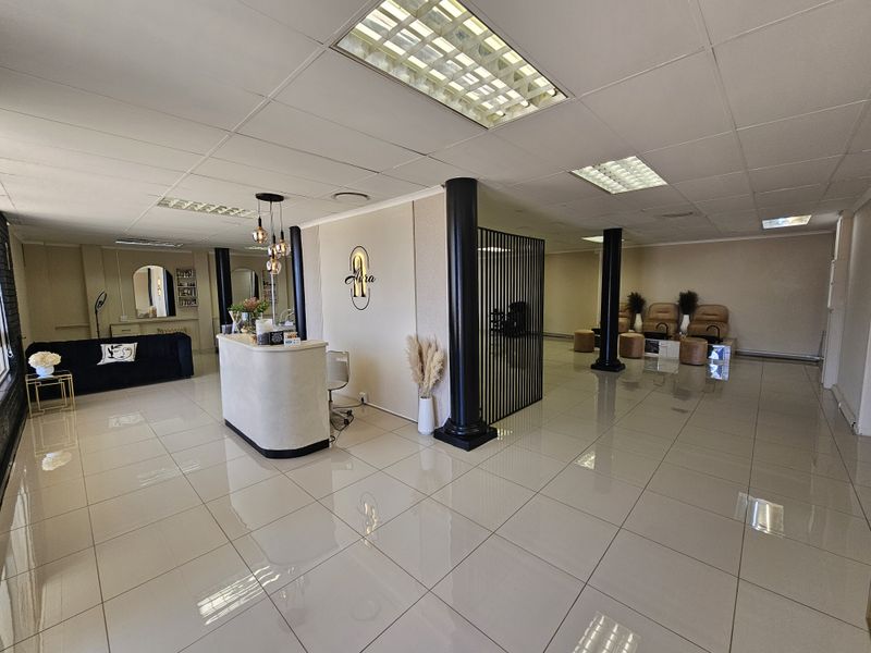 Spacious open-plan retail salon area featuring polished tile flooring, recessed ceiling lighting, structural support columns, and a dedicated reception desk.