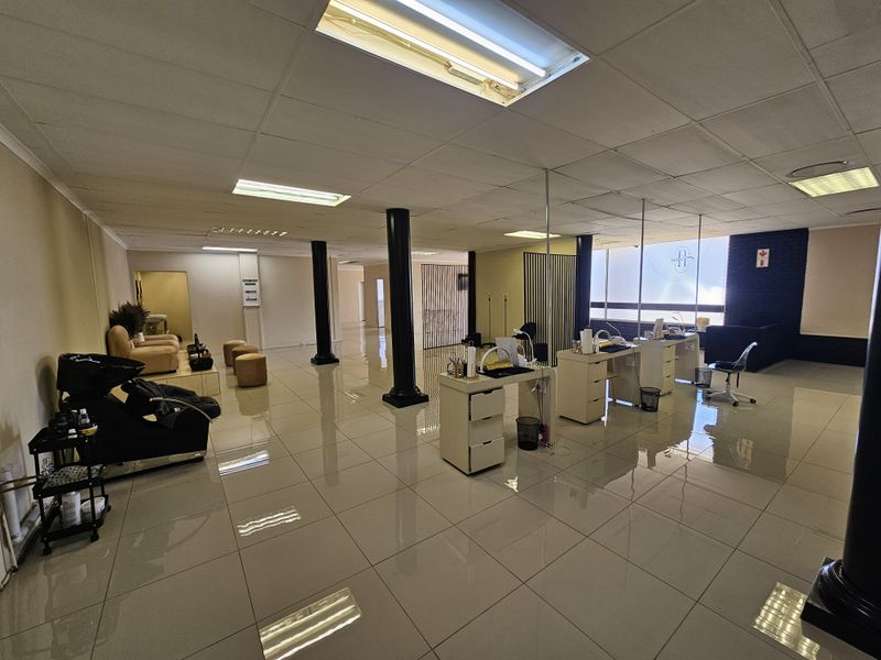 Spacious open-plan retail or salon space featuring polished tile flooring, recessed ceiling lighting, and structural support columns.
