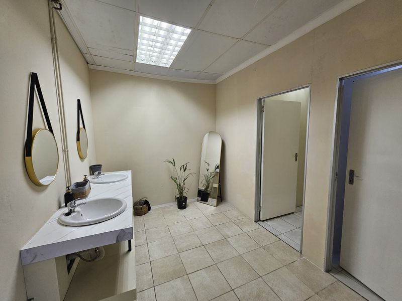 A functional commercial bathroom featuring a double vanity with integrated sinks, tiled flooring, and drop ceiling lighting.