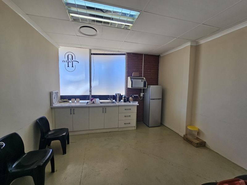 A functional kitchenette area featuring built-in cabinetry, a stainless steel sink, and a tiled drop ceiling in a commercial retail space.