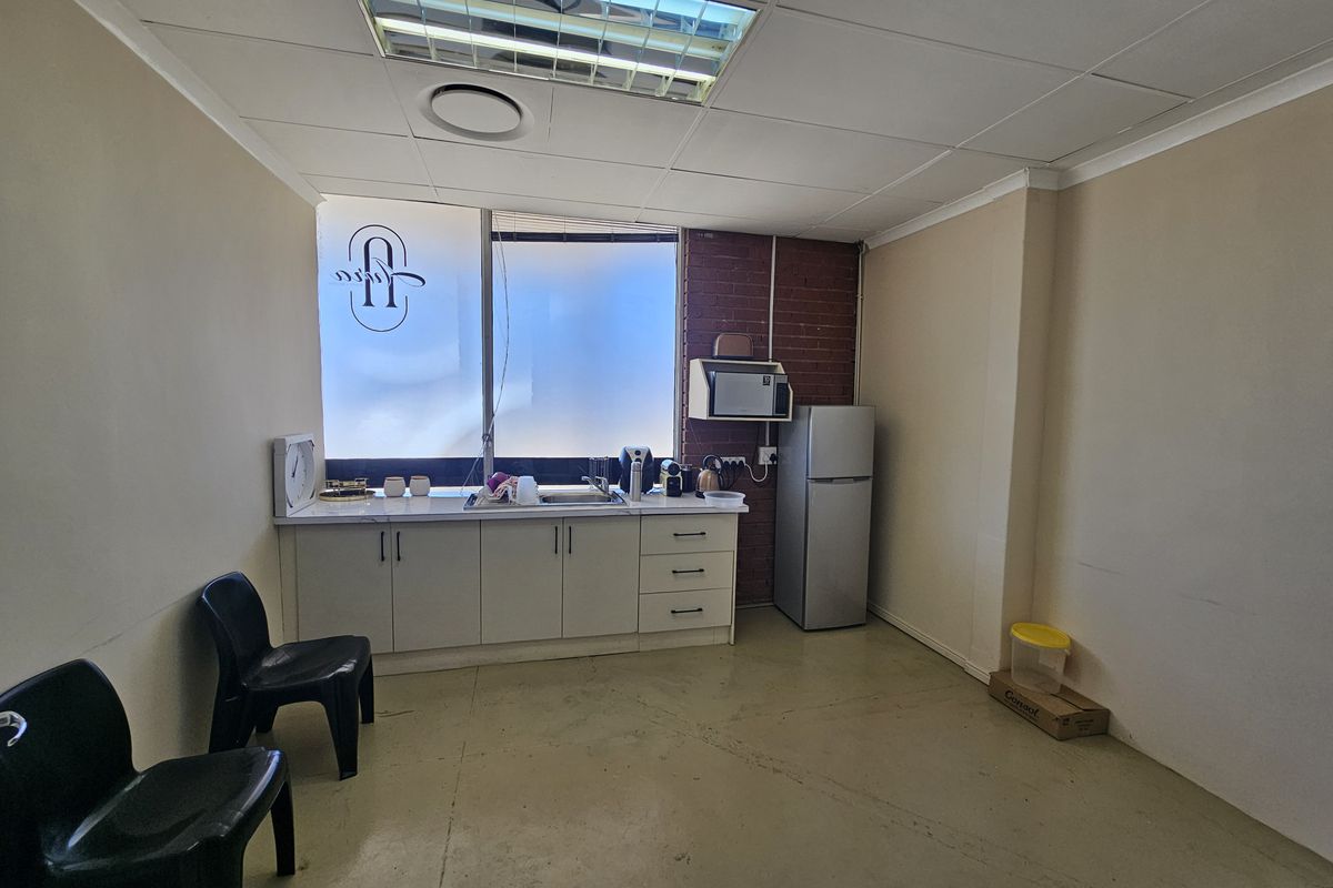A functional kitchenette area featuring built-in cabinetry, a stainless steel sink, and a tiled drop ceiling in a commercial retail space.