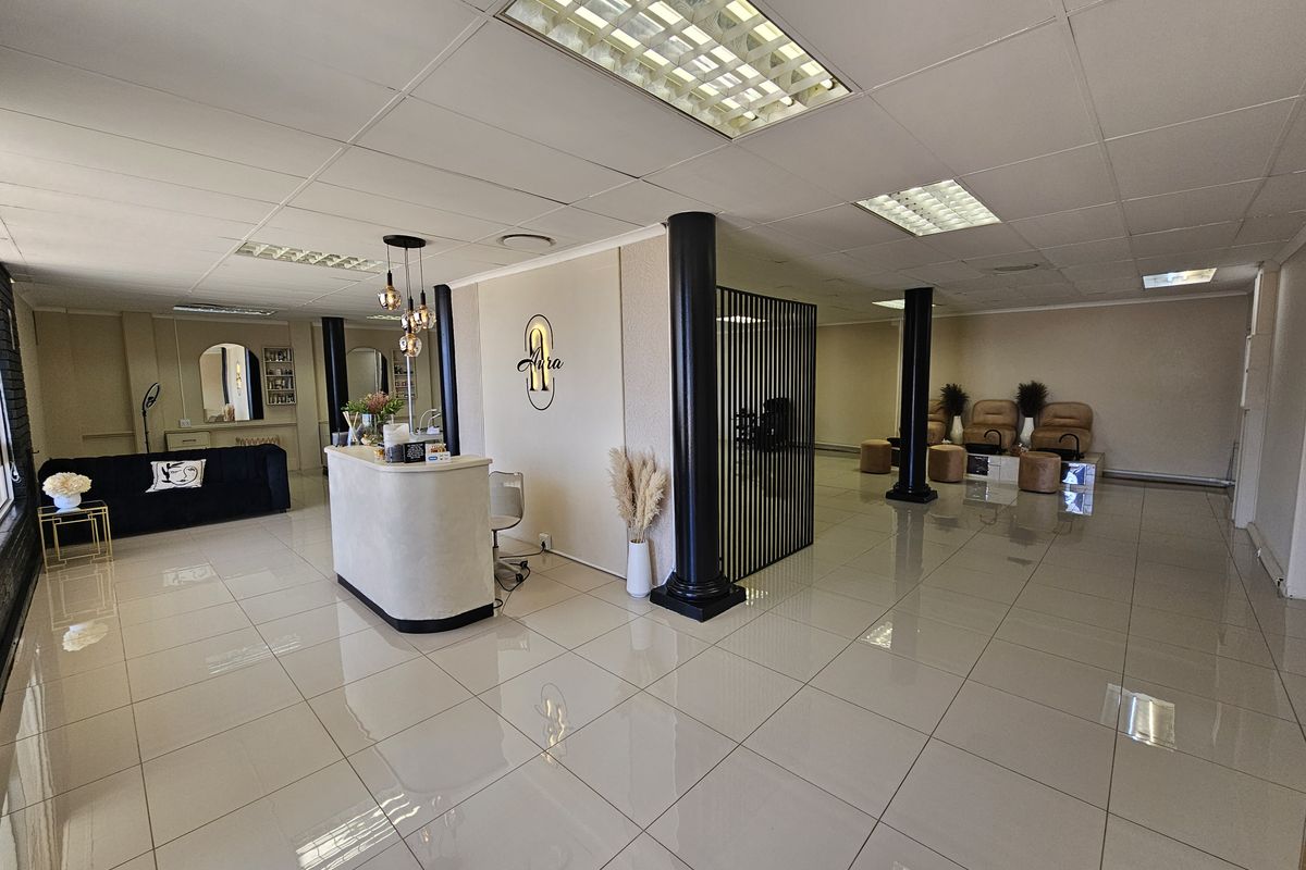 Spacious open-plan retail salon area featuring polished tile flooring, recessed ceiling lighting, structural support columns, and a dedicated reception desk.