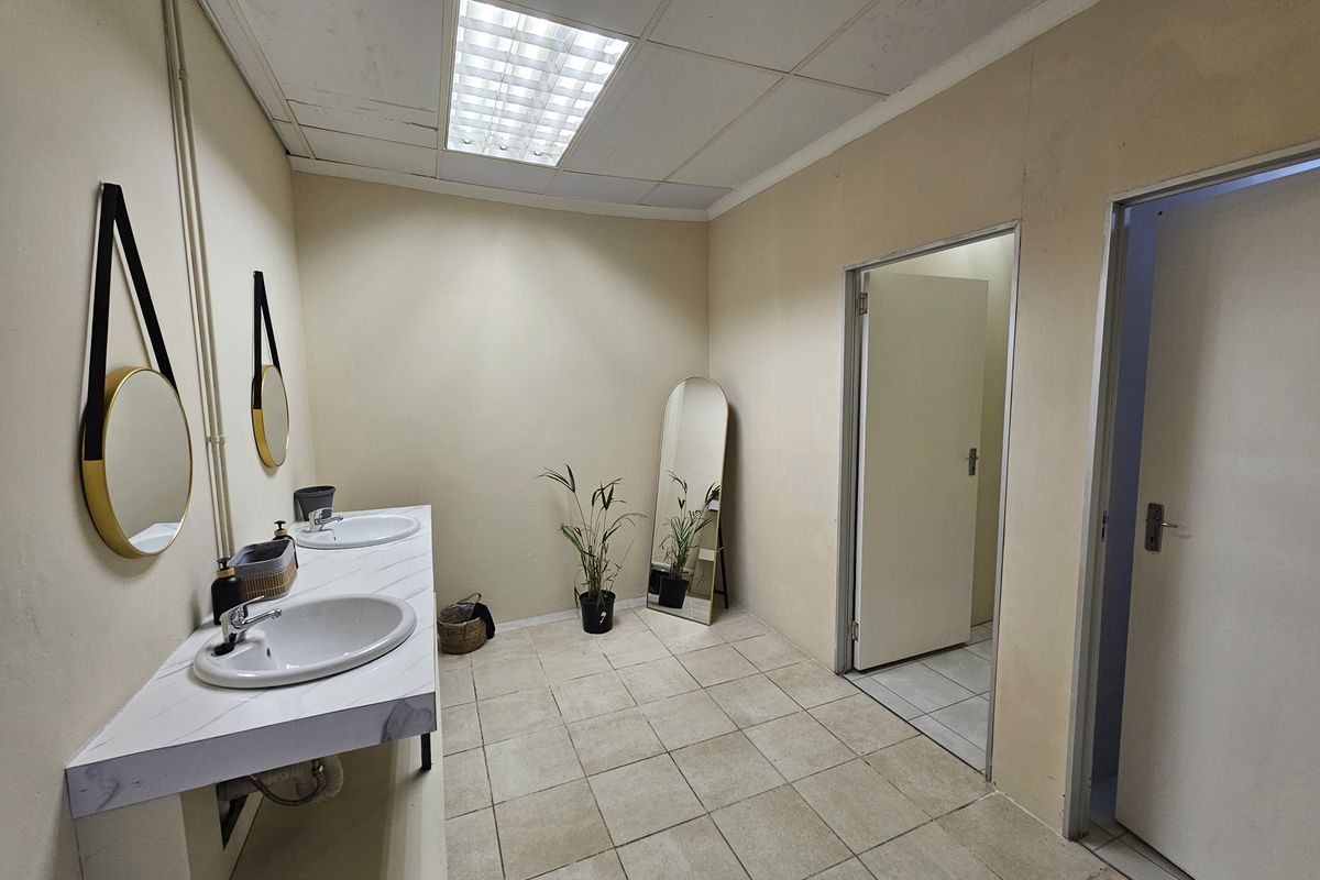A functional commercial bathroom featuring a double vanity with integrated sinks, tiled flooring, and drop ceiling lighting.