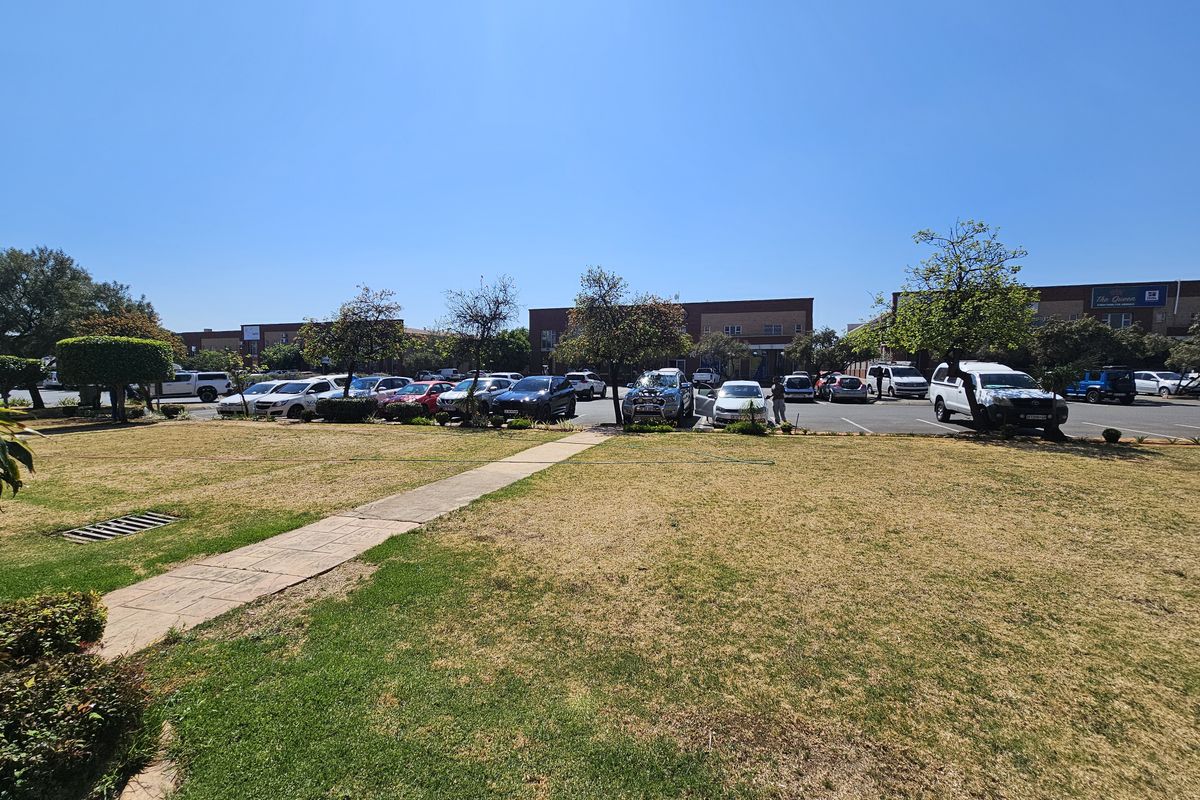 A view of the retail property exterior featuring a landscaped lawn area leading to a paved parking lot with multiple vehicle bays.
