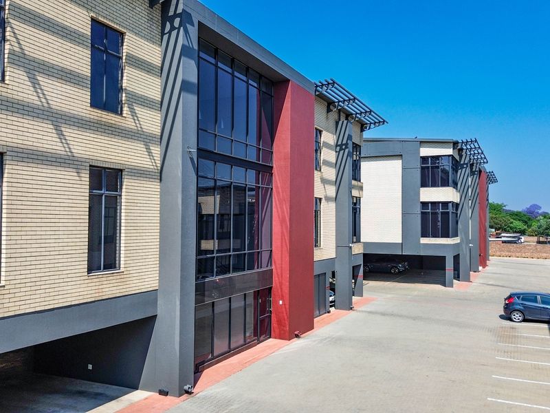 Modern multi-story office building featuring a contemporary brick and glass facade with integrated covered parking and paved exterior access.