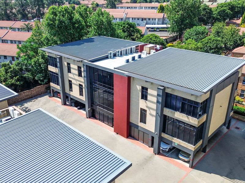 Aerial view of a modern multi-story office building featuring a brick and glass facade, metal roofing, and integrated covered parking facilities.