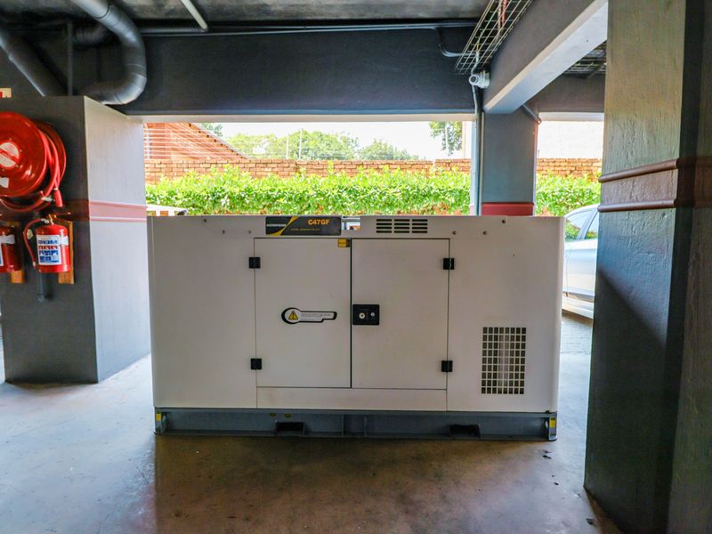 Utility area featuring a soundproof diesel generator, fire safety equipment, and exposed industrial ceiling infrastructure.