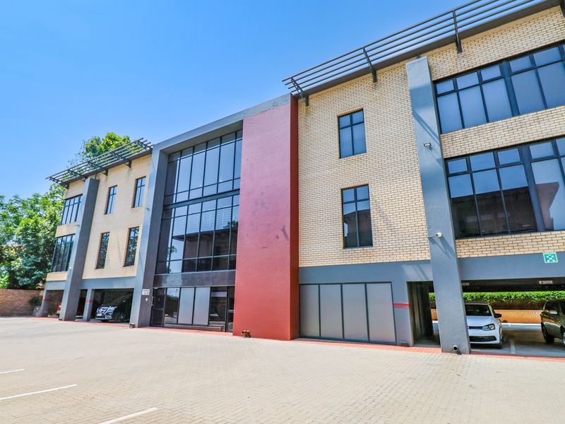 Modern multi-story office building featuring a brick and glass facade with integrated covered parking and a paved exterior approach.