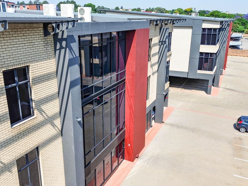 Aerial view of a modern multi-story office building featuring brick and glass facade elements with an adjacent paved parking lot.