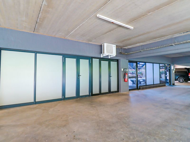 A spacious, clean garage area featuring concrete ceilings, frosted glass office-style doors, and integrated air conditioning, suitable for professional or utility use.