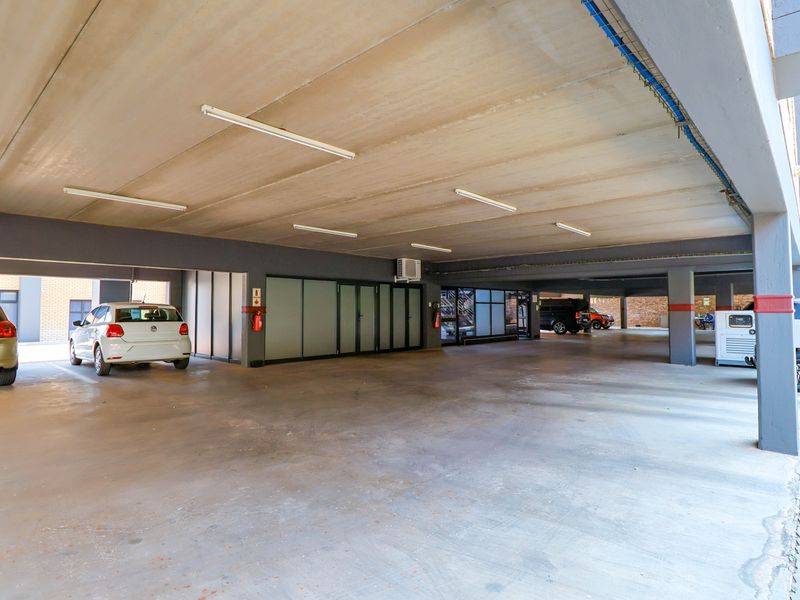 A spacious covered parking garage featuring concrete flooring, structural columns, fluorescent lighting, and integrated fire safety equipment.