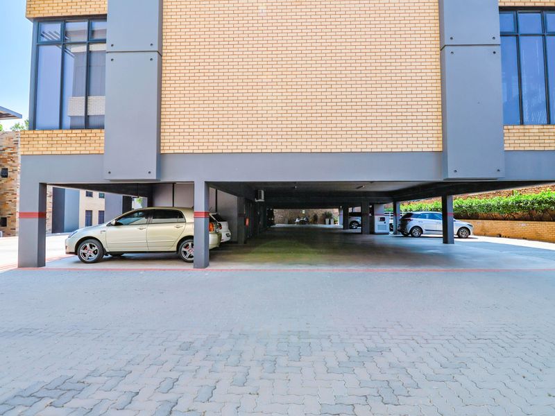 A modern office building featuring a covered ground-level parking area with brick and concrete structural elements and paved driveway access.