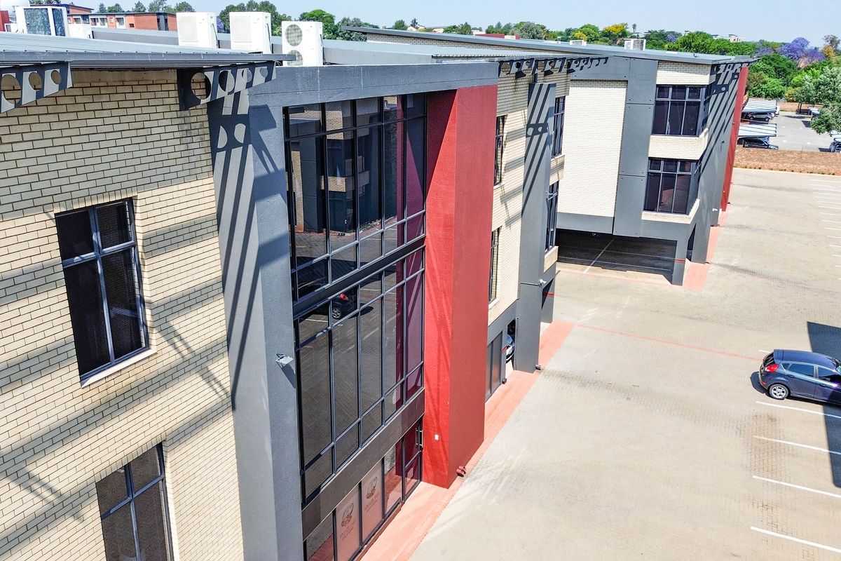 Aerial view of a modern multi-story office building featuring brick and glass facade elements with an adjacent paved parking lot.