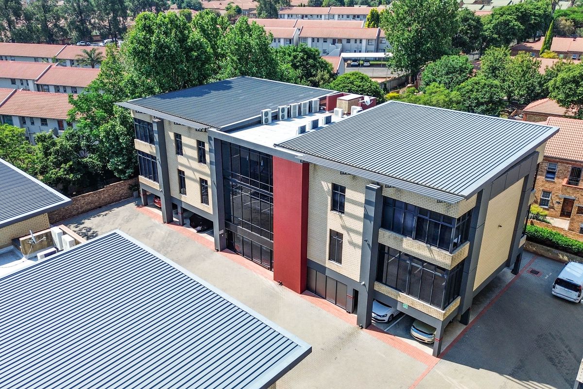 Aerial view of a modern multi-story office building featuring a brick and glass facade, metal roofing, and integrated covered parking facilities.