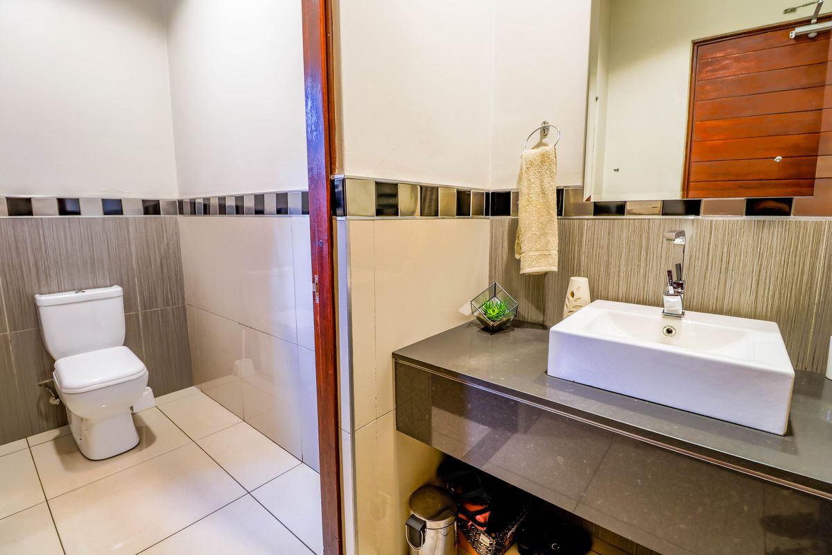Modern bathroom featuring a sleek vanity with a stone countertop, basin, and a separate toilet area with contemporary wall tiling.
