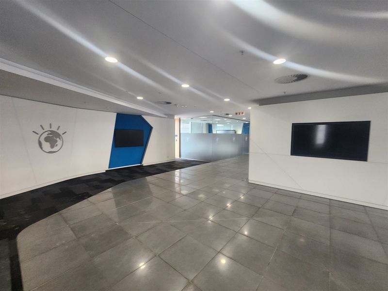 Modern open-plan office reception area featuring tiled and carpeted flooring, recessed lighting, and glass partitioning for a professional workspace environment.
