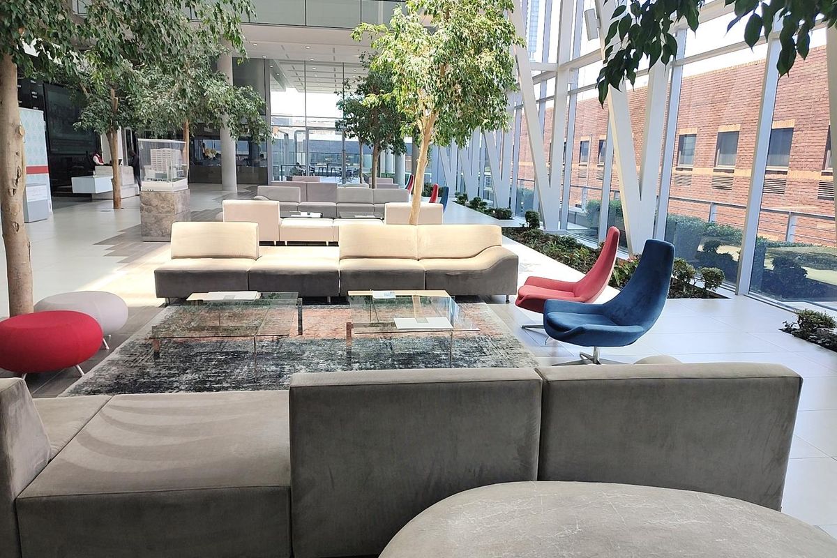 Spacious modern office atrium featuring floor-to-ceiling glass windows, tiled flooring, and integrated indoor greenery in a bright, open-plan professional environment.