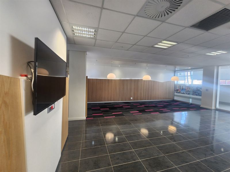 A spacious, modern open-plan office area featuring a mix of tiled and carpeted flooring, wood-paneled feature walls, and integrated ceiling lighting.