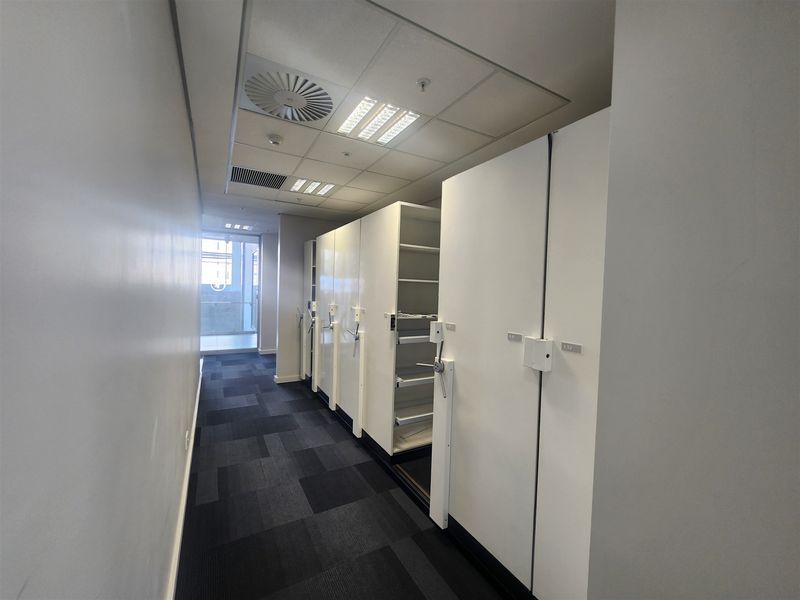 A functional utility space featuring a mobile shelving system, carpeted flooring, and a suspended ceiling with integrated lighting and air conditioning.