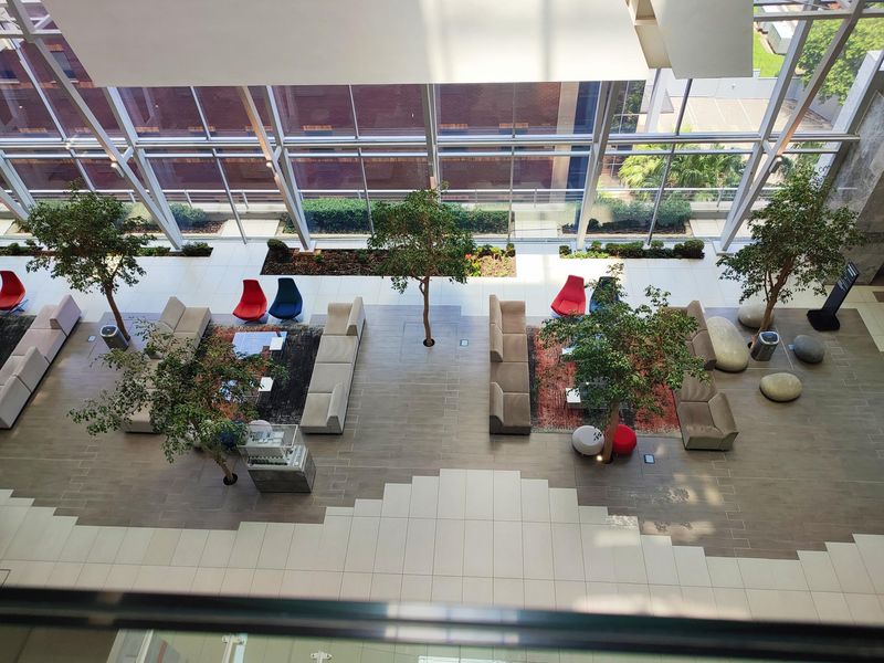 A spacious, modern office atrium featuring floor-to-ceiling glass walls, tiled flooring, and integrated indoor landscaping, creating a bright and professional environment.