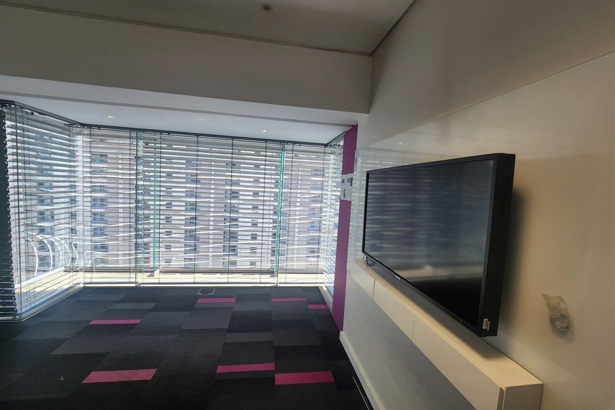 Modern office space featuring floor-to-ceiling windows with venetian blinds, patterned carpet tiles, and a sleek wall-mounted media console.