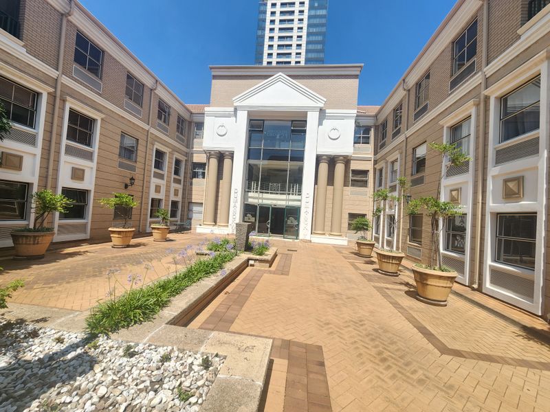 A well-maintained office building courtyard featuring paved walkways, classical architectural columns, and a central glass entrance facade.