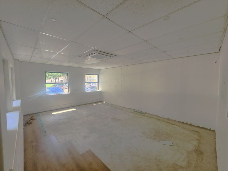 An empty office space featuring a suspended ceiling, integrated air conditioning, and large windows, currently requiring flooring and wall finishing.