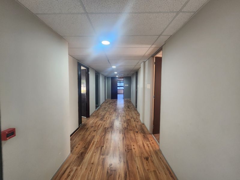 A clean, well-lit office hallway featuring wood-look laminate flooring and a suspended ceiling with recessed lighting, providing access to multiple office suites.