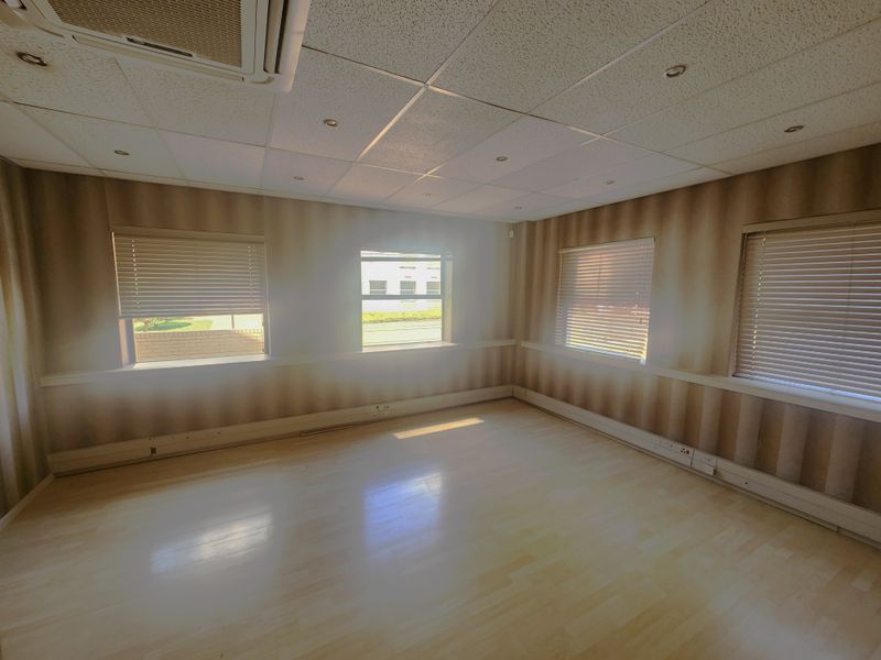 Empty office space featuring laminate flooring, suspended ceiling with recessed lighting, integrated air conditioning, and multiple windows with fitted venetian blinds.