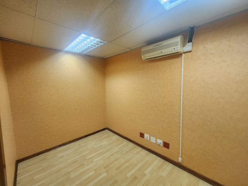 A vacant office space featuring laminate flooring, a suspended ceiling with recessed lighting, and a wall-mounted air conditioning unit.
